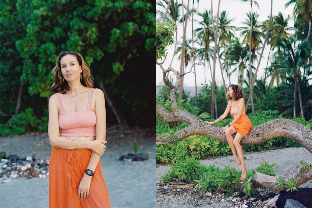 A woman in an orange skirt sitting on a palm tree on the beach surrounded my tropical nature, captured by a Big Island Hawaii portrait photographer.