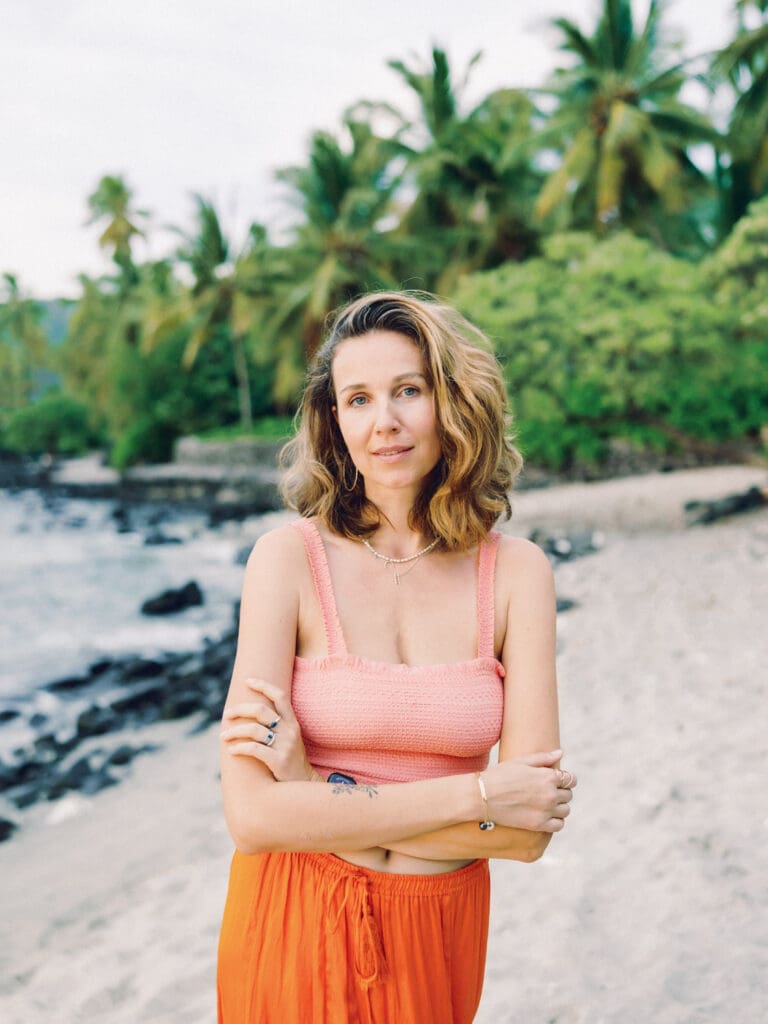 A woman in an orange skirt poses on the beach surrounded my tropical palm trees, captured by a Big Island Hawaii portrait photographer.