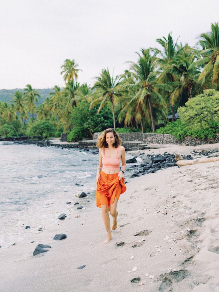 A woman in an orange skirt running on the beach surrounded my tropical palm trees, captured by a Big Island Hawaii portrait photographer.