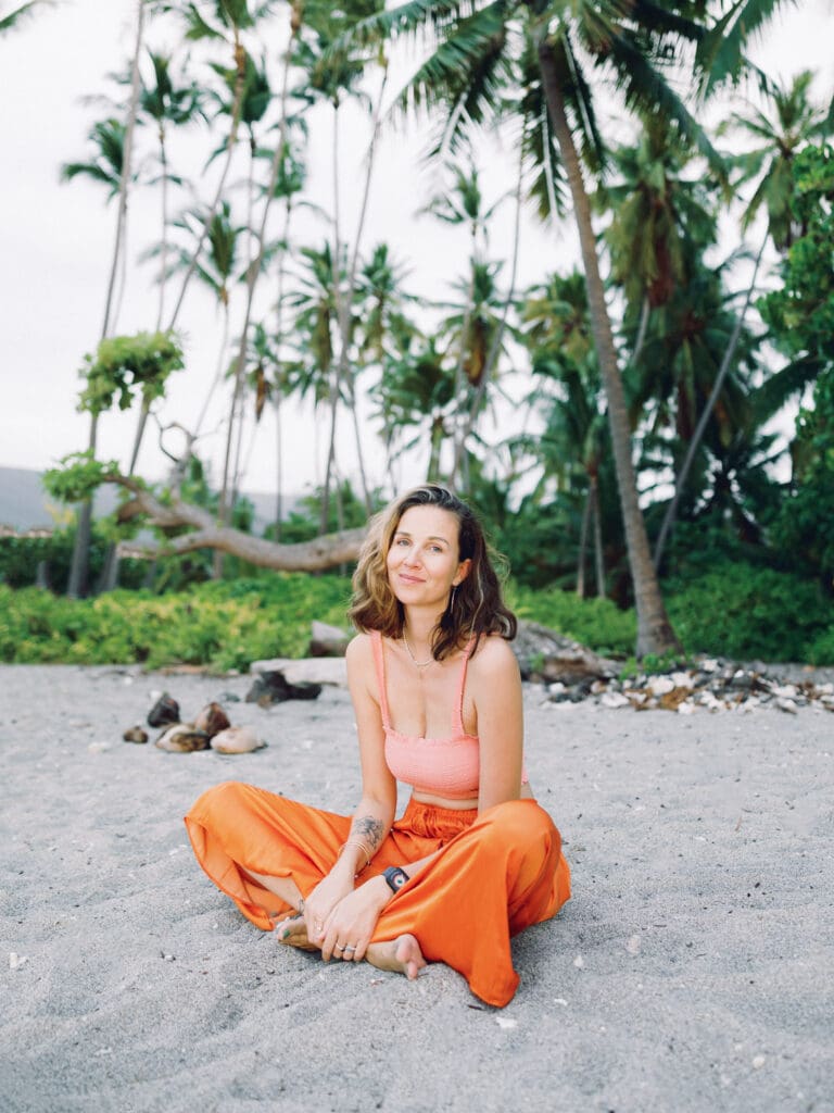 A woman in an orange skirt poses on the beach surrounded my tropical palm trees, captured by a Big Island Hawaii portrait photographer.