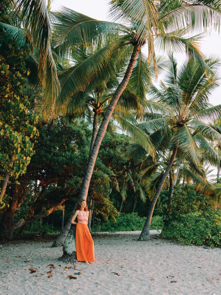 A woman in an orange skirt poses beside a palm tree, captured by a Big Island Hawaii portrait photographer.