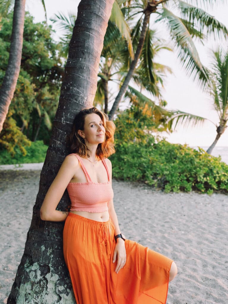 A woman in an orange skirt poses beside a palm tree, captured by a Big Island Hawaii portrait photographer.