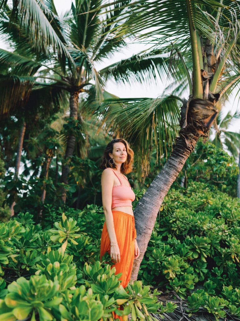 A woman in an orange skirt poses beside a palm tree, captured by a Big Island Hawaii portrait photographer.