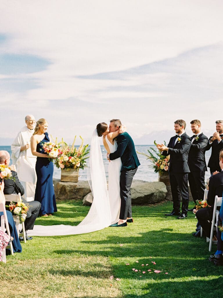 Bride and groom first kiss at a beautiful beach wedding ceremony at Gar Woods, Lake Tahoe, featuring a stunning backdrop of the lake and mountains.