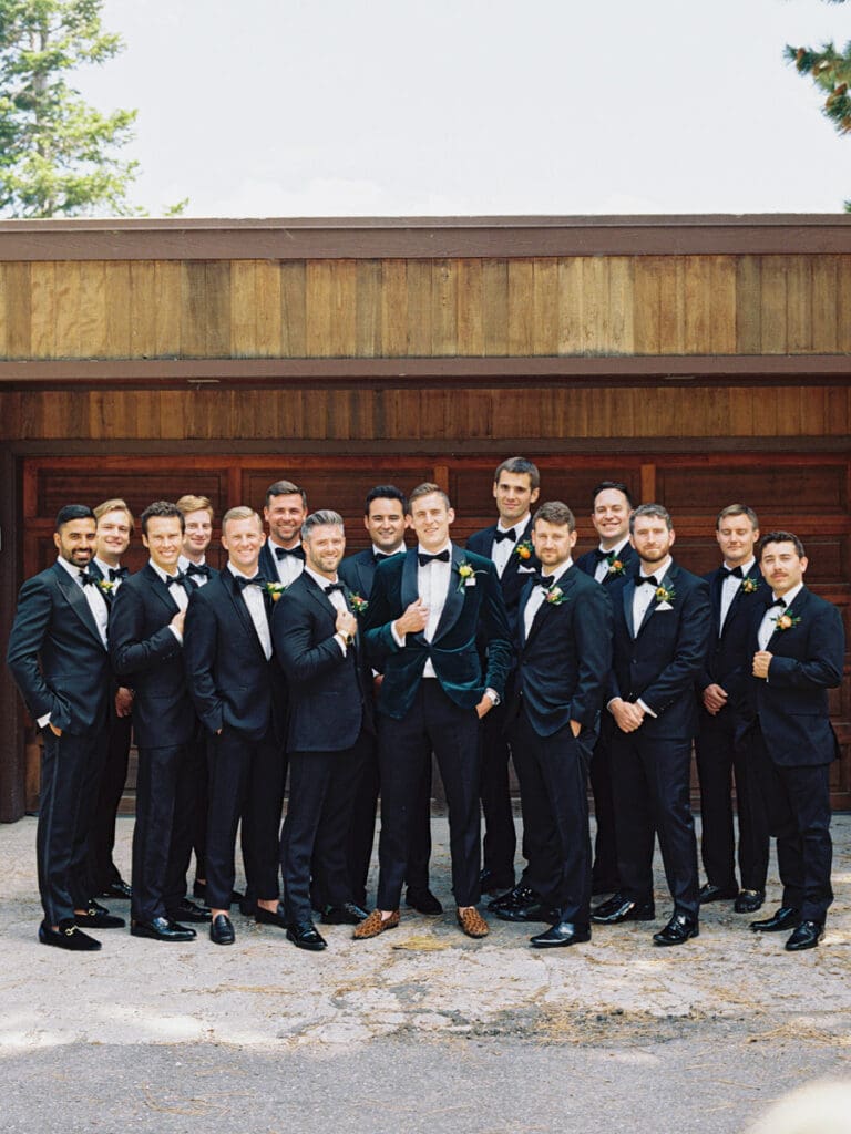 Groomsmen in tuxedos pose together for a photo against a rustic wooden wall at Gar Woods Lake Tahoe Wedding.