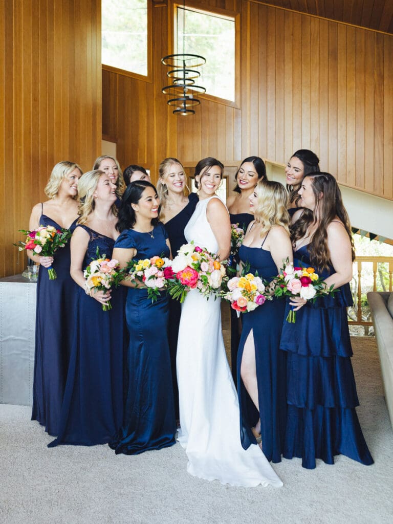 Bridesmaids in navy dresses pose together for a photo against a rustic wooden wall at Gar Woods Lake Tahoe Wedding.