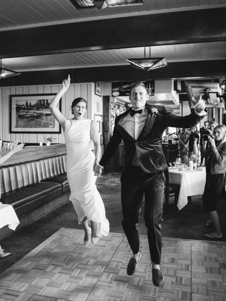 A joyful bride and groom leap in the air, celebrating their wedding reception at Gar Woods Lake Tahoe.