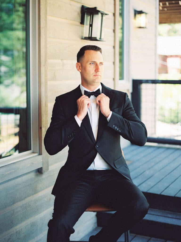 A stylish groom in a tuxedo relaxes on a chair, showcasing a charming portrait at Gar Woods Lake Tahoe wedding.