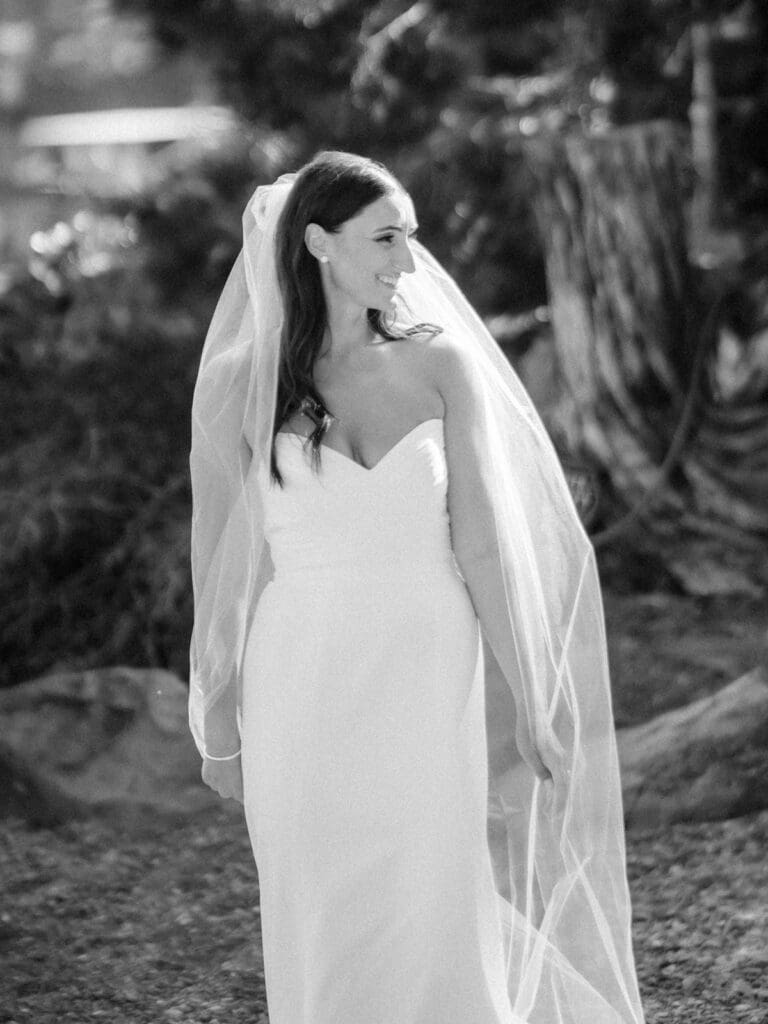 A beautiful bride in a white gown and veil poses gracefully along a scenic path at Gar Woods, Lake Tahoe, radiating joy.