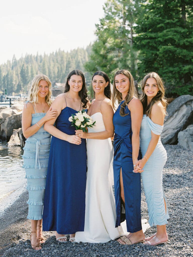 A stunning beach photo of bride and bridesmaids in blue dresses, radiating happiness at Gar Woods Lake Tahoe wedding.