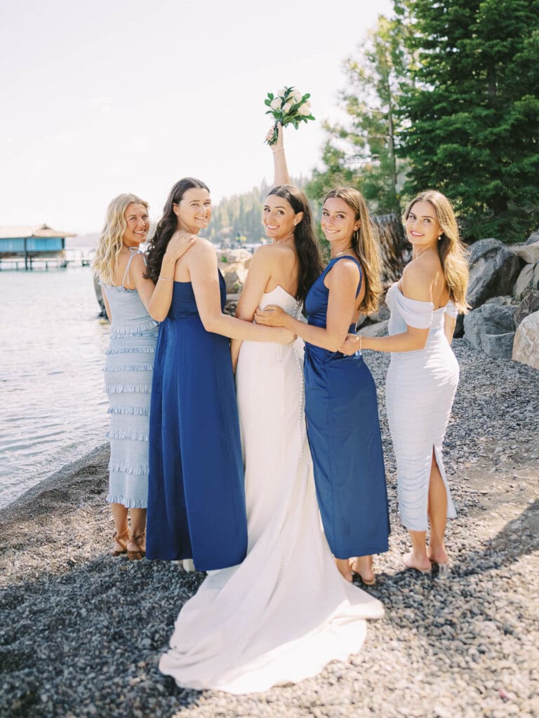 A stunning beach photo of bride and bridesmaids in blue dresses, radiating happiness at Gar Woods Lake Tahoe wedding.