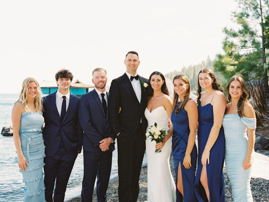 A joyful group of groomsmen and bridesmaids in blue dresses stands side by side, celebrating at a wedding at Gar Woods, Lake Tahoe.