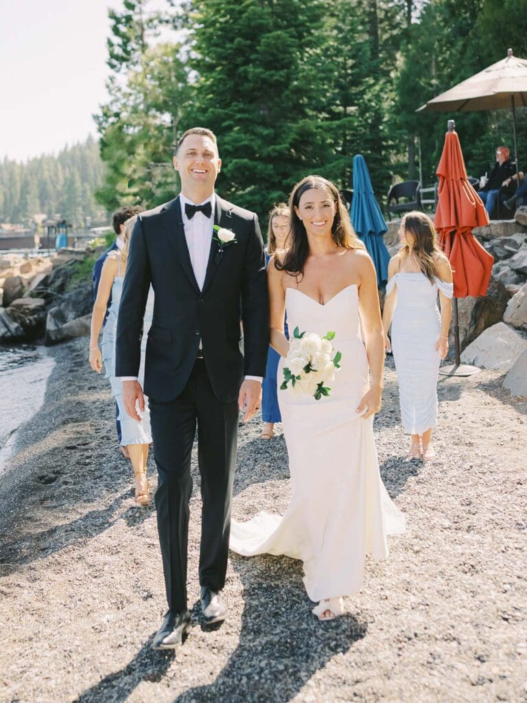 A joyful group of groomsmen and bridesmaids in blue dresses walking, celebrating at a wedding at Gar Woods, Lake Tahoe.