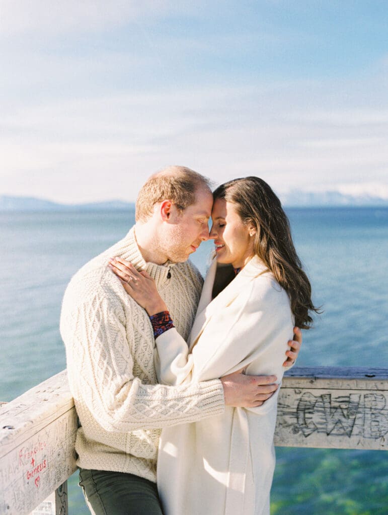 A photo of a couple on the dock cuddling and smiling at each other during Lake Tahoe Winter Engagement Shoot