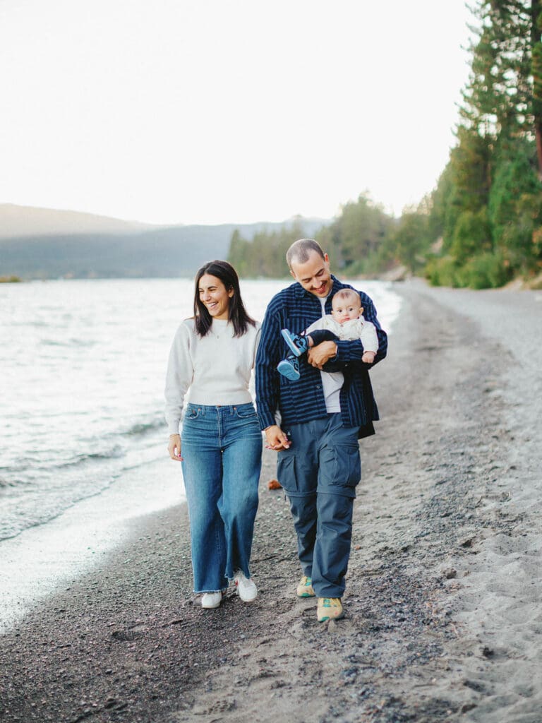 A joyful family walks on the Lake Tahoe beach, creating memories with their baby during a sunset.