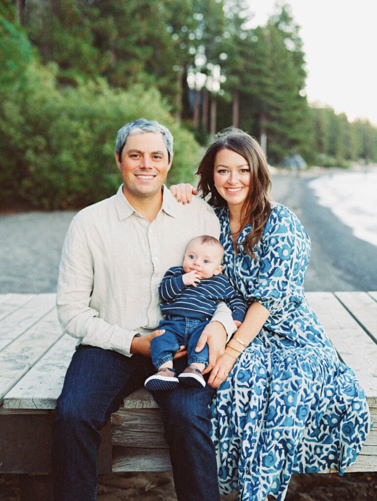 A joyful family sitting on Lake Tahoe dock, creating memories with their baby during a sunset.