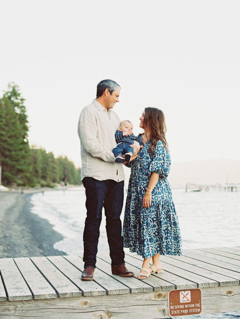 A joyful family standing on Lake Tahoe dock, creating memories with their baby during a sunset.