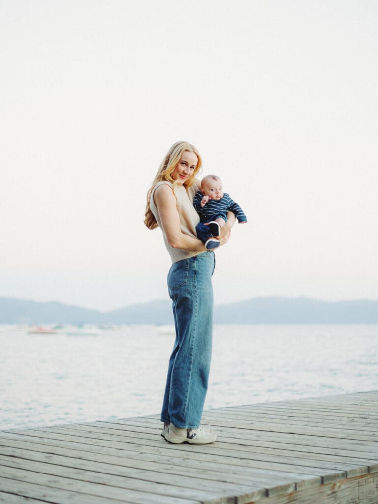 A joyful family poses on the Lake Tahoe beach, creating memories with their baby during a sunset.