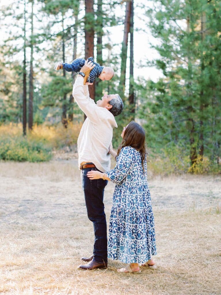 A family of three poses together in a lush field surrounded by trees during their Lake Tahoe photo session.