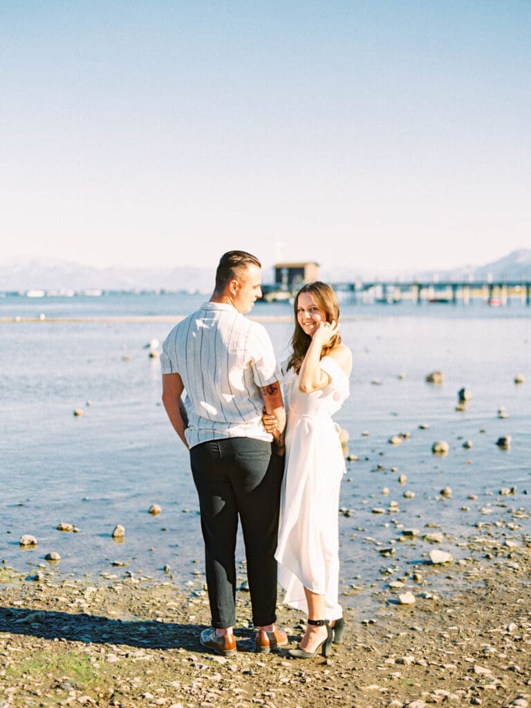 A couple enjoys a romantic engagement session by the serene waters of Lake Tahoe, surrounded by stunning natural beauty.