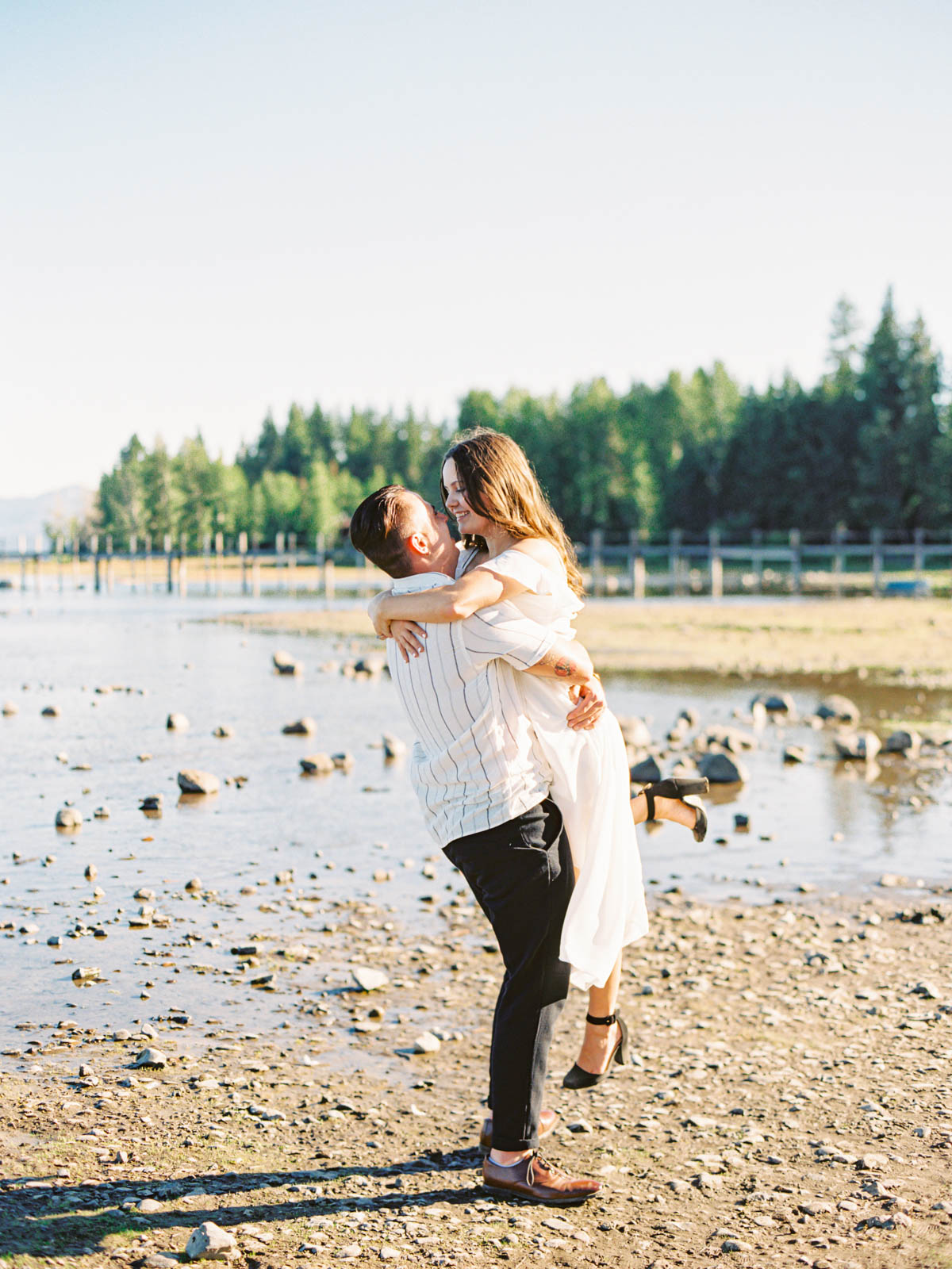 A couple enjoys a romantic engagement session by the serene waters of Lake Tahoe, surrounded by stunning natural beauty.