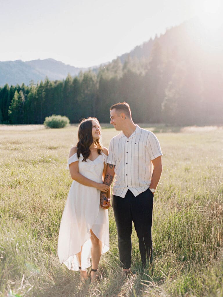 A couple strolls hand in hand through a mountain field during their Lake Tahoe engagement photo session.