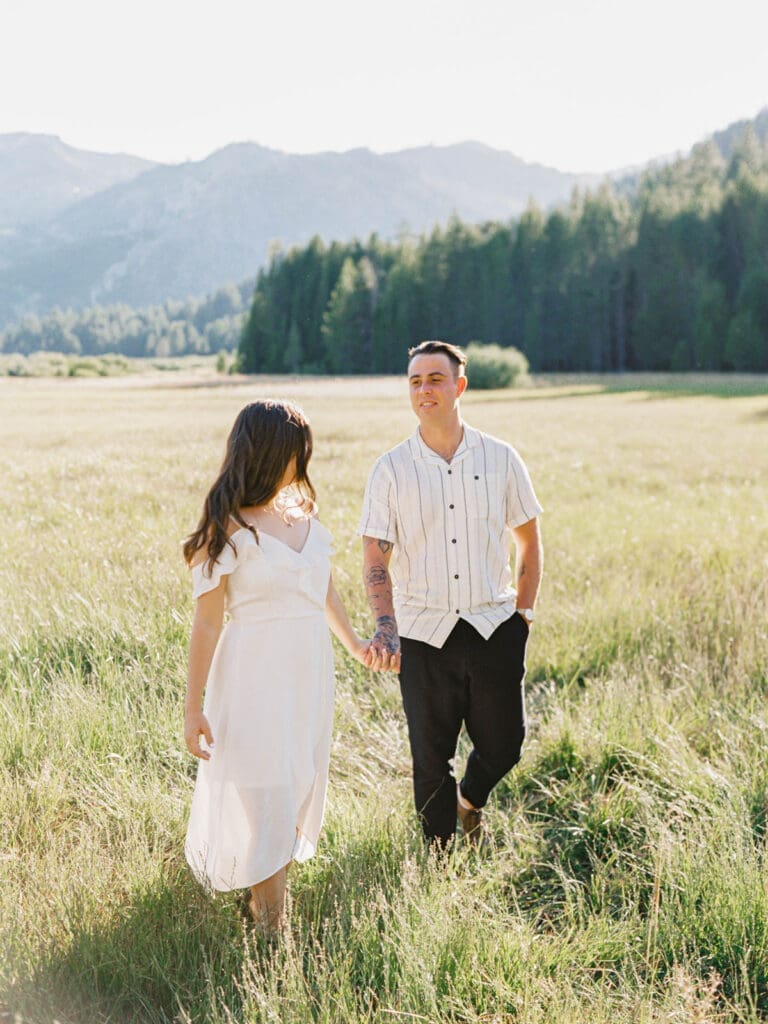 A couple strolls hand in hand through a mountain field during their Lake Tahoe engagement photo session.