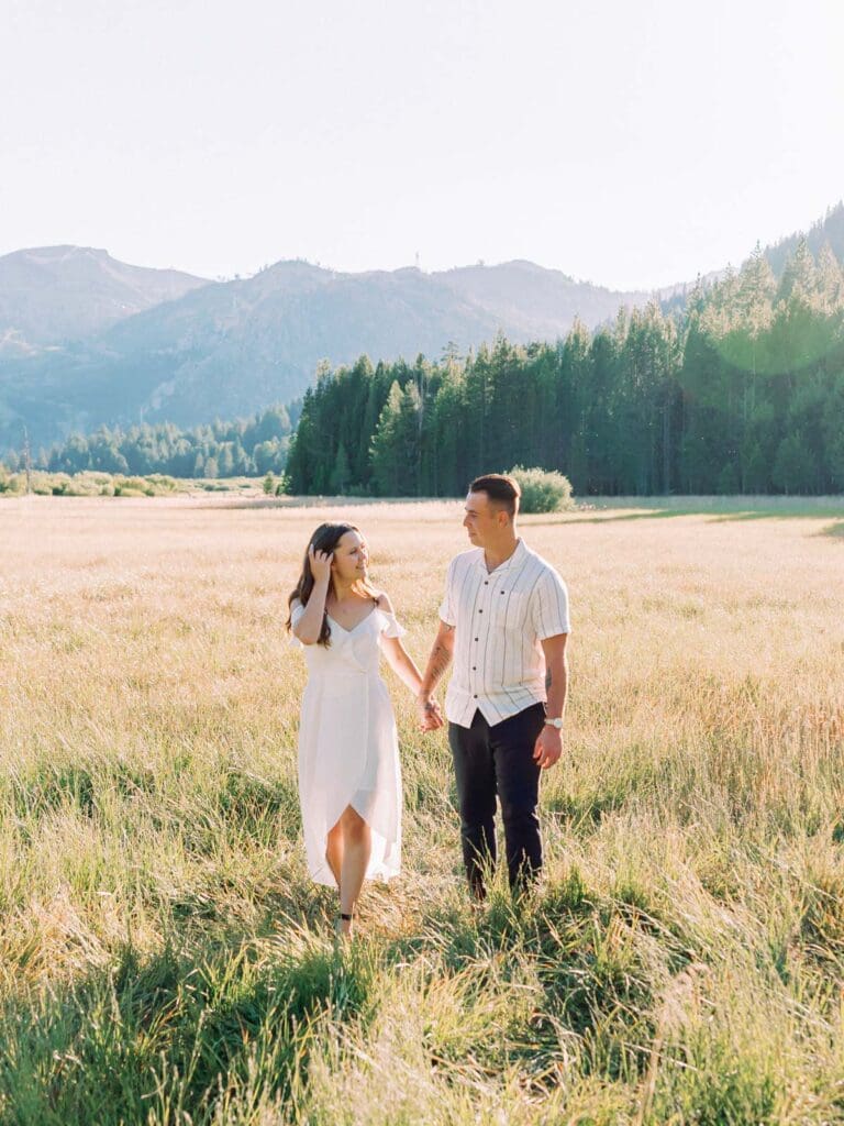 A couple strolls hand in hand through a mountain field during their Lake Tahoe engagement photo session.