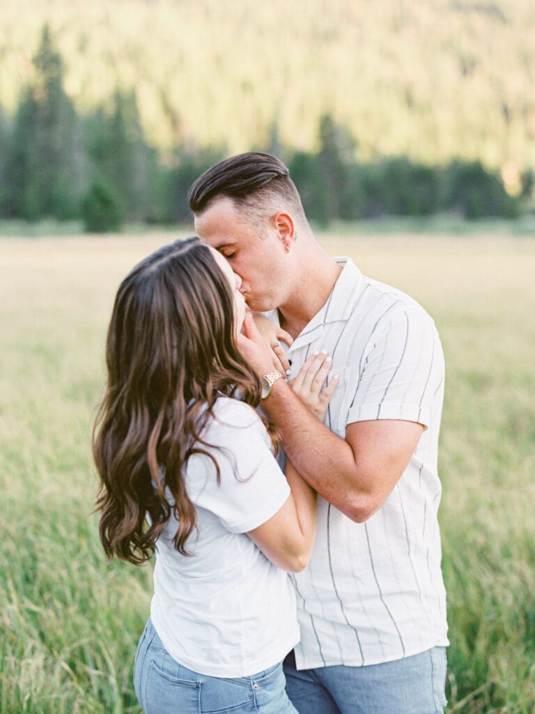 A couple kisses at a mountain field during their Lake Tahoe engagement photo session.