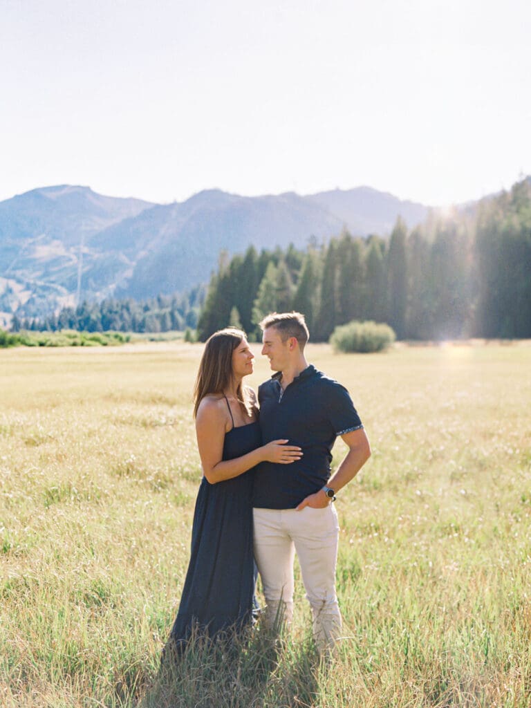 An engaged couple enjoys a serene moment in a field, with the stunning Lake Tahoe mountains in the distance.