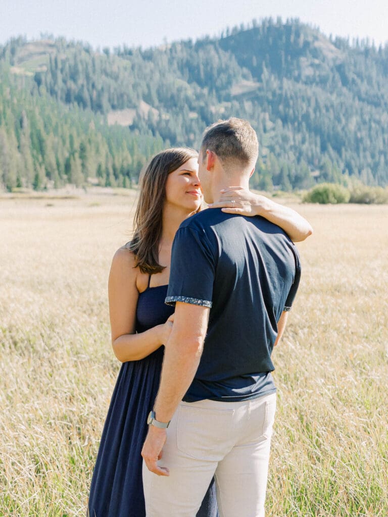 An engaged couple enjoys a serene moment in a field, with the stunning Lake Tahoe mountains in the distance.