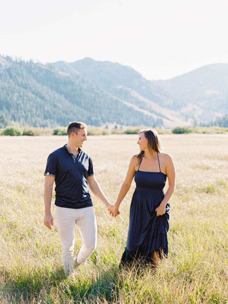 An engaged couple walking together in a vibrant field, with the majestic Lake Tahoe mountains in the background.