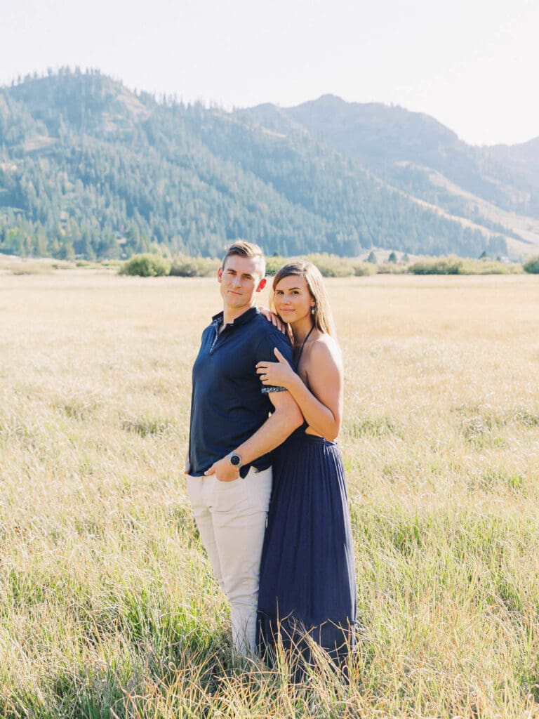 In a vibrant mountain meadow, a couple celebrates their engagement with the beautiful Lake Tahoe mountains behind them.