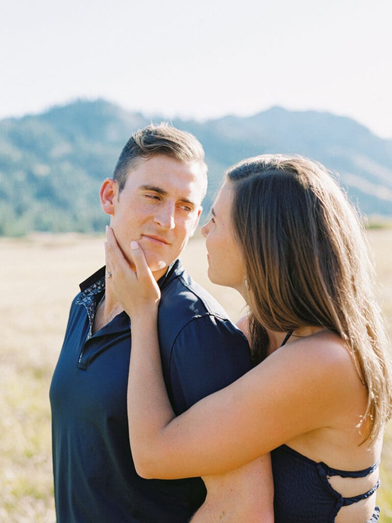 An engaged couple enjoys a serene moment in a field, with the stunning Lake Tahoe mountains in the distance.