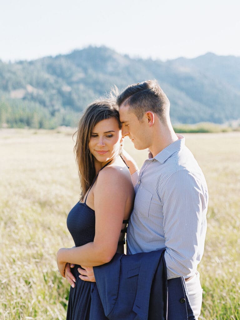 An engaged couple stands together in a vibrant field, with the majestic Lake Tahoe mountains in the background.