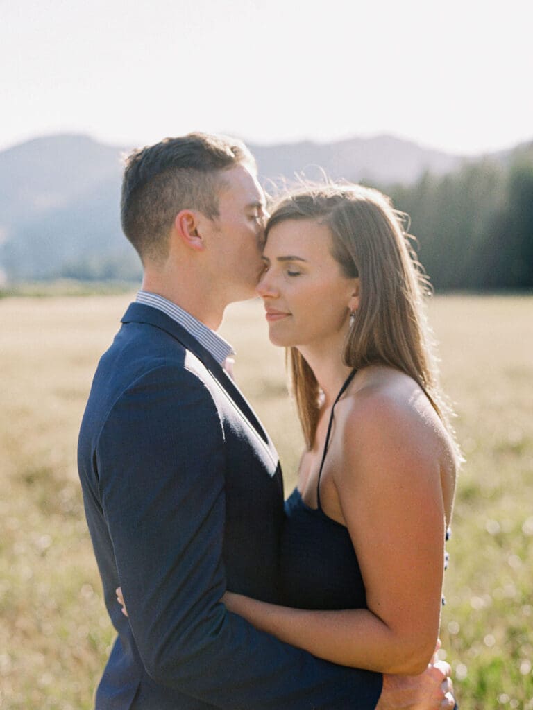 A couple pose in a picturesque field, capturing their engagement amidst the stunning Lake Tahoe mountains.