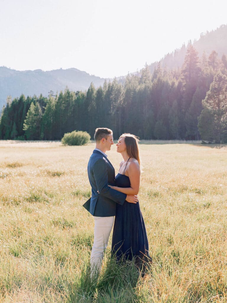 A couple shares a moment in a picturesque field, with the beautiful Lake Tahoe mountains serving as a backdrop for their engagement.