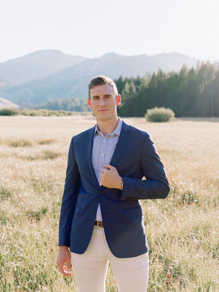 An engaged man dressed in a blue suit poses in a vibrant field, with the majestic Lake Tahoe mountains in the background.