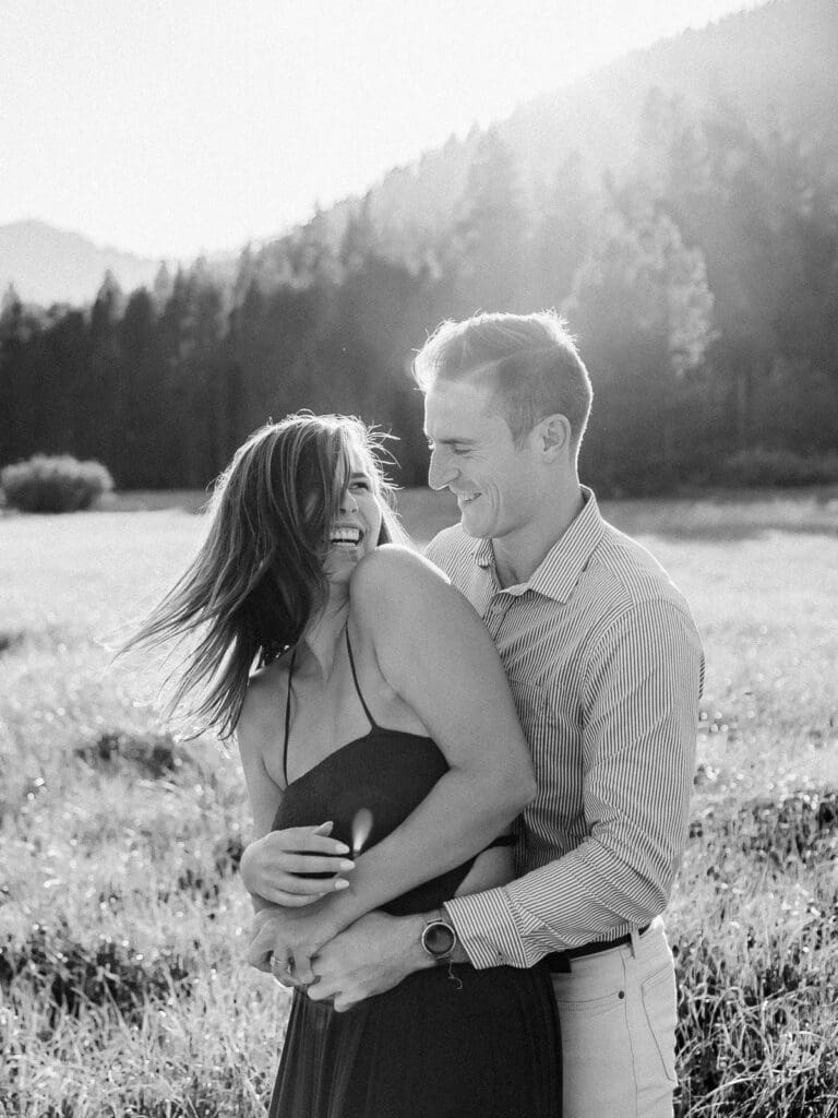 A couple having fun in a picturesque field, with the beautiful Lake Tahoe mountains serving as a backdrop for their engagement.