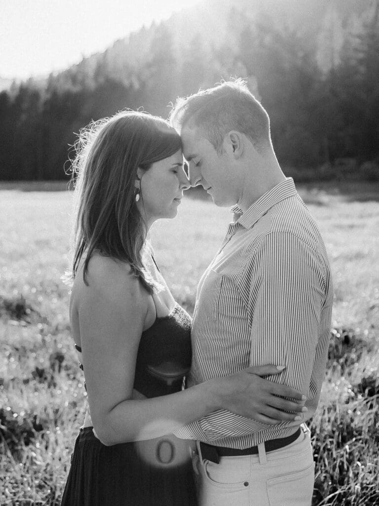 A couple is standing head to head in a lush alpine field, capturing their engagement amidst the majestic Lake Tahoe mountains.