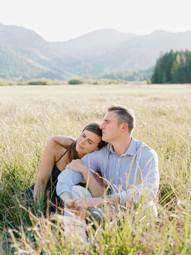 A couple is sitting in a lush alpine field, capturing their engagement amidst the majestic Lake Tahoe mountains.