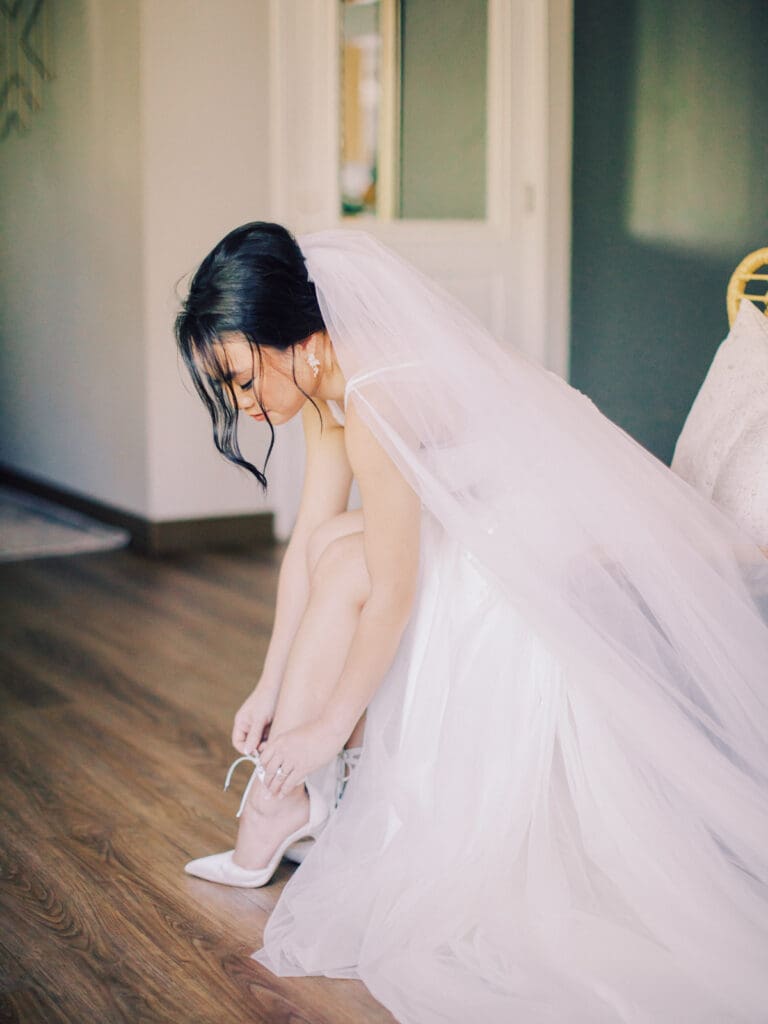 A bride in a wedding dress ties her shoes while preparing for her wedding at Tannenbaum Lake Tahoe.