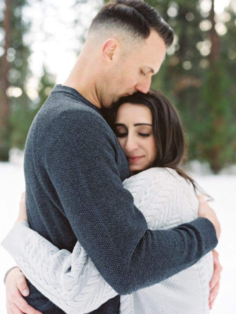 A couple embraces in a snowy landscape during their engagement session in Lake Tahoe, surrounded by serene winter scenery.