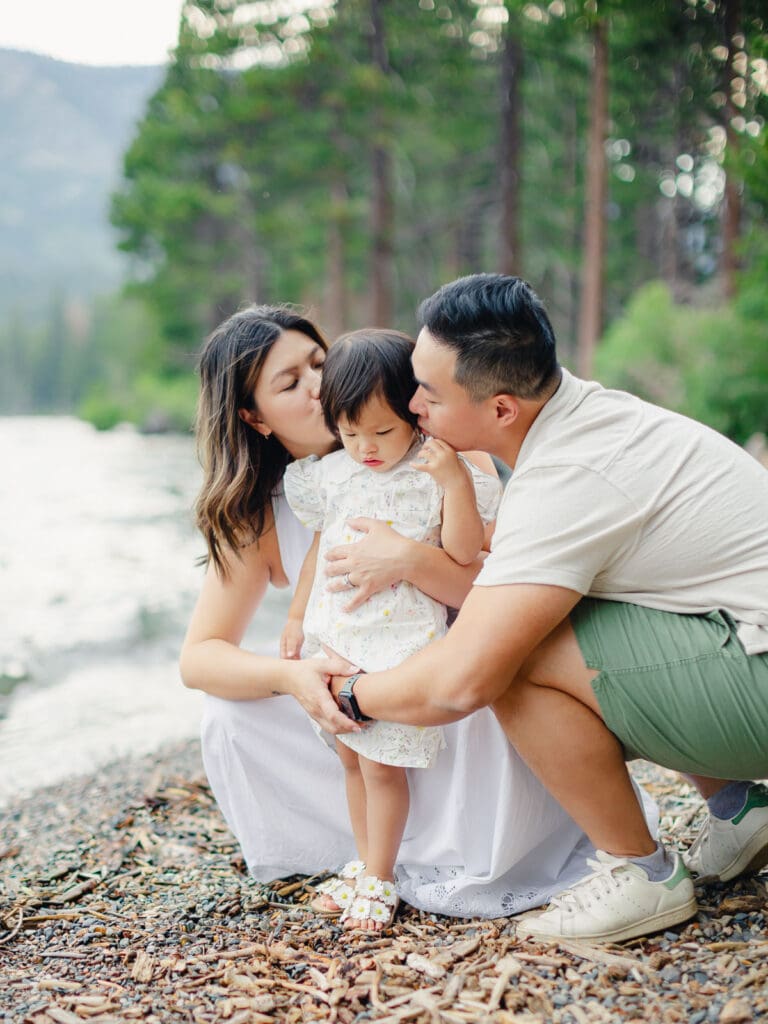 Parents holds her baby on the beach, with South Lake Tahoe's tranquil waters behind them during a family photography session.