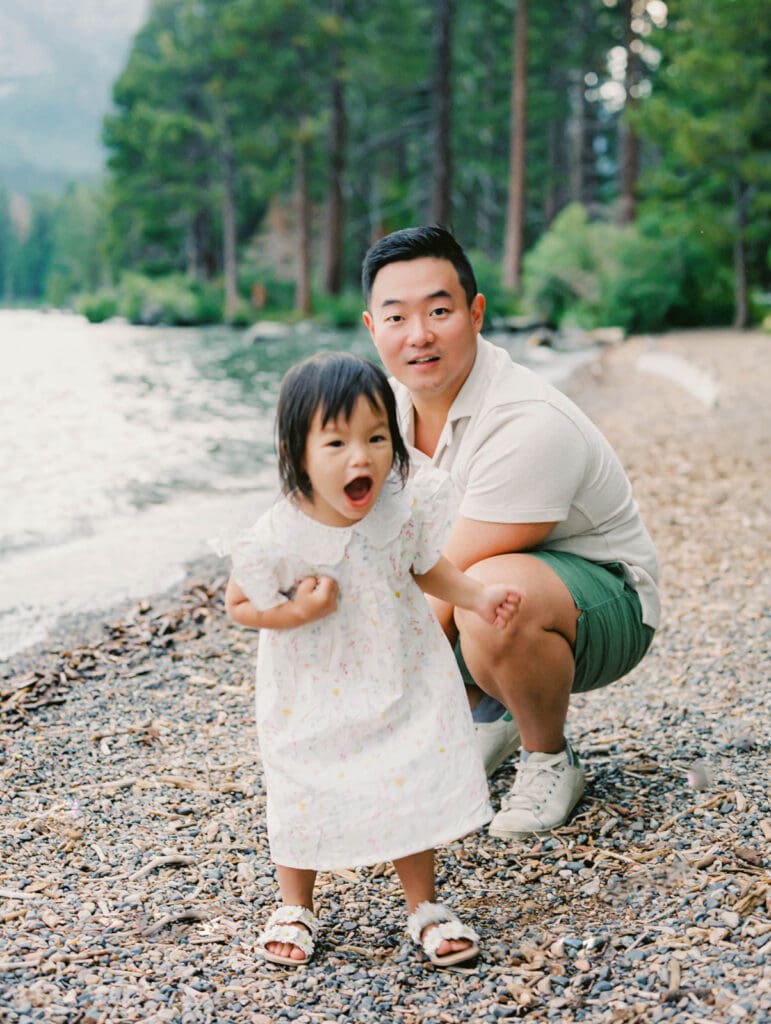 A father plays with his baby on the beach, with South Lake Tahoe's tranquil waters behind them during a family photography session.