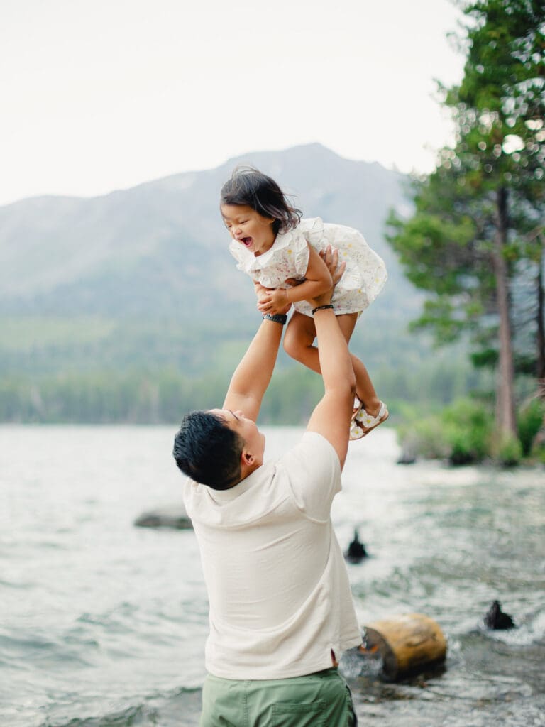 A father plays with his baby on the beach, with South Lake Tahoe's tranquil waters behind them during a family photography session.