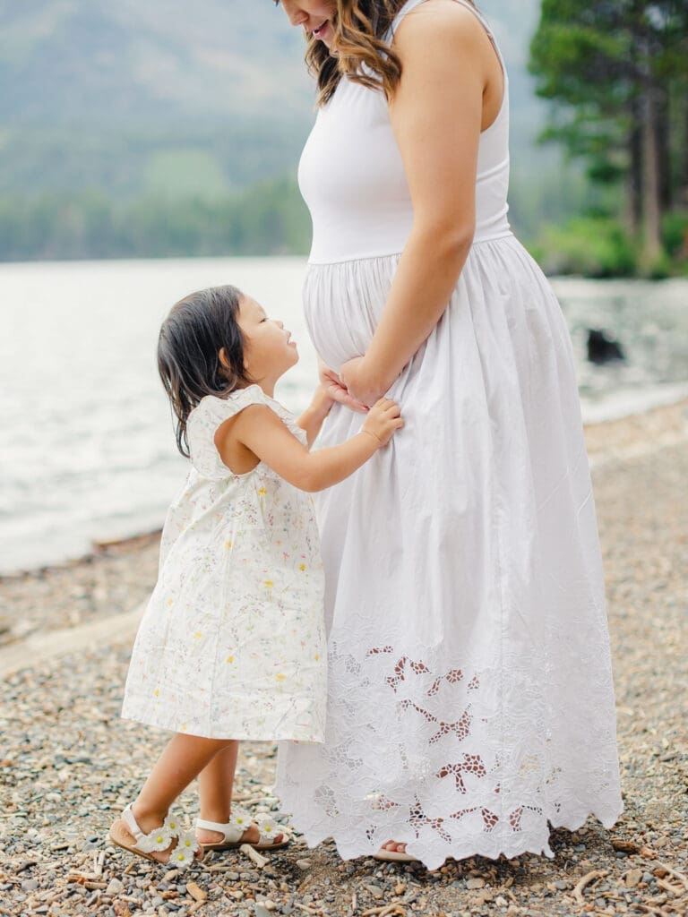 A mother holds her baby on the beach, with South Lake Tahoe's tranquil waters behind them during a maternity photography session.