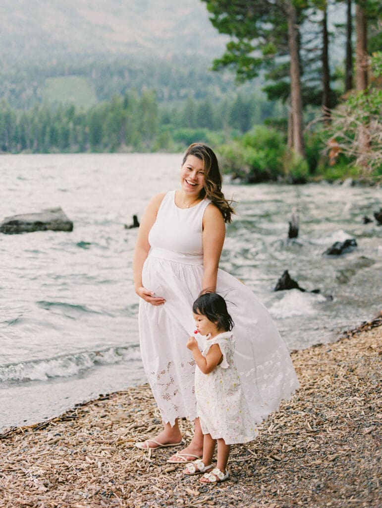 A mother holds her baby on the beach, with South Lake Tahoe's tranquil waters behind them during a family photography session.