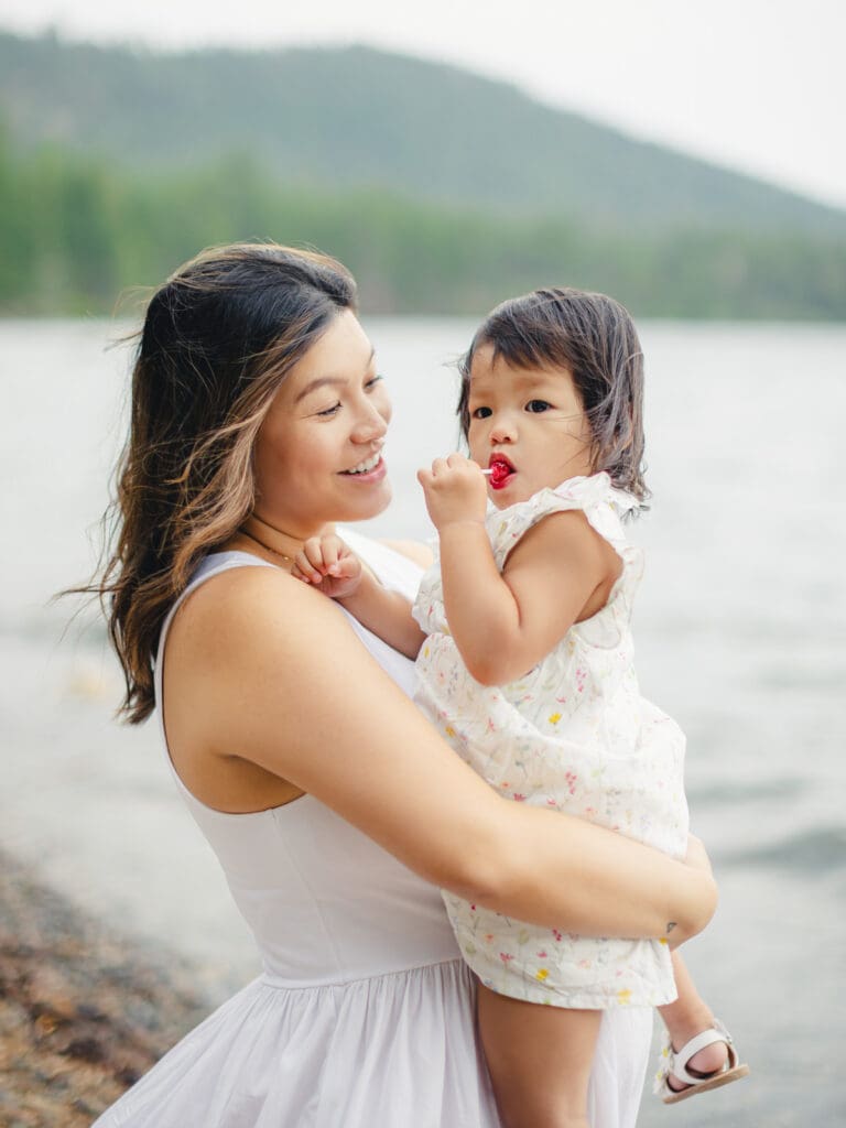 A mother holds her baby on the beach, with South Lake Tahoe's tranquil waters behind them during a family photography session.