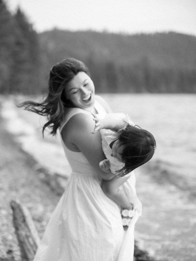 A mother holds her baby on the beach, with South Lake Tahoe's tranquil waters behind them during a family photography session.